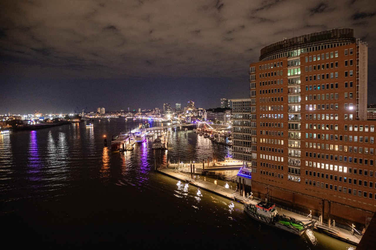 Aerial night view of Hamburg’s HafenCity district with illuminated waterfront buildings, boats, and the Elbe River.
