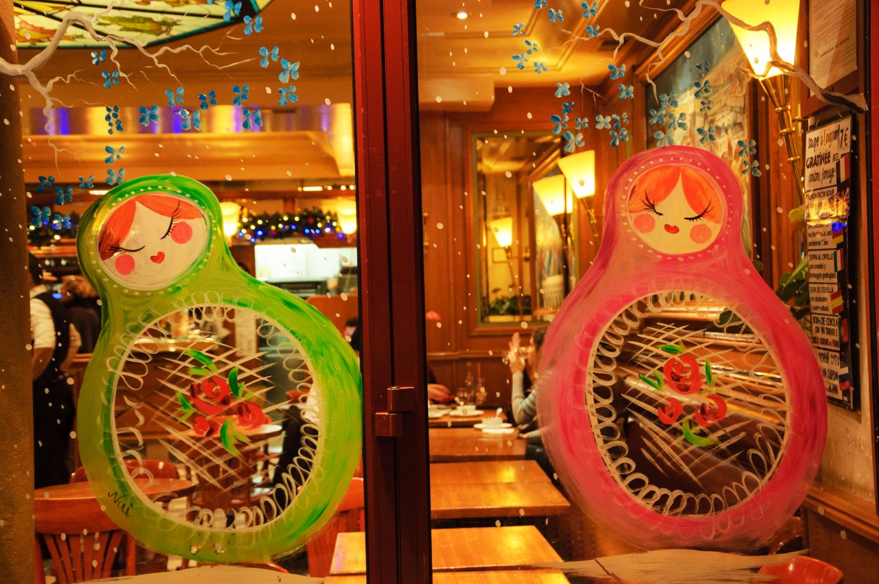 Parisian cafe windows decorated for Christmas with colorful matryoshka dolls and snowflakes.