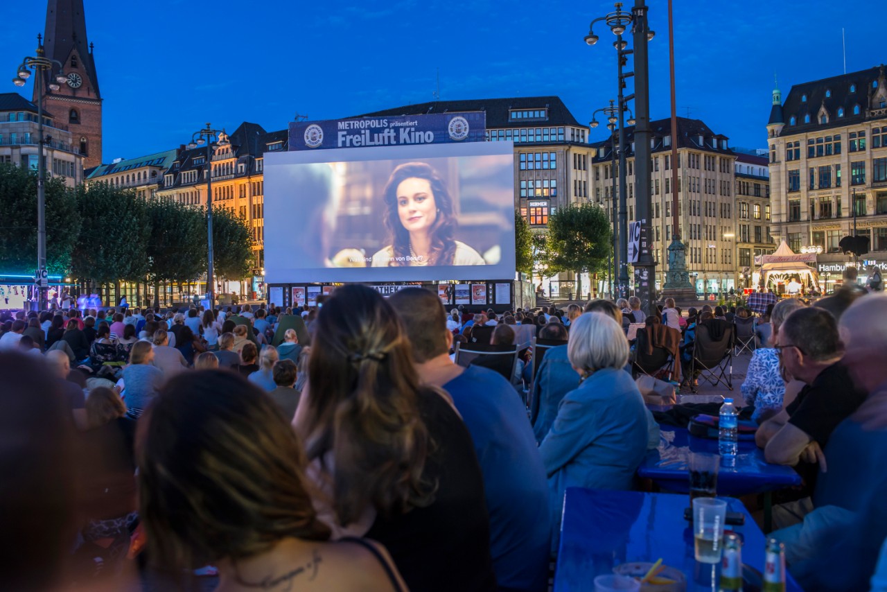 The main square in Hamburg, people sit and watch a public projection of the film