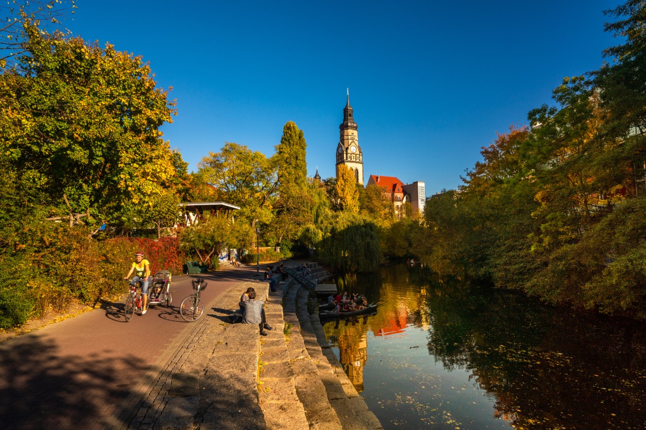 Leipzig view showing Karl Heine Canal, church, bell tower, people riding boat in the canal or river, trees, buildings, bicycle and people sitting on the stairs near on the canal in the Plagwitz area