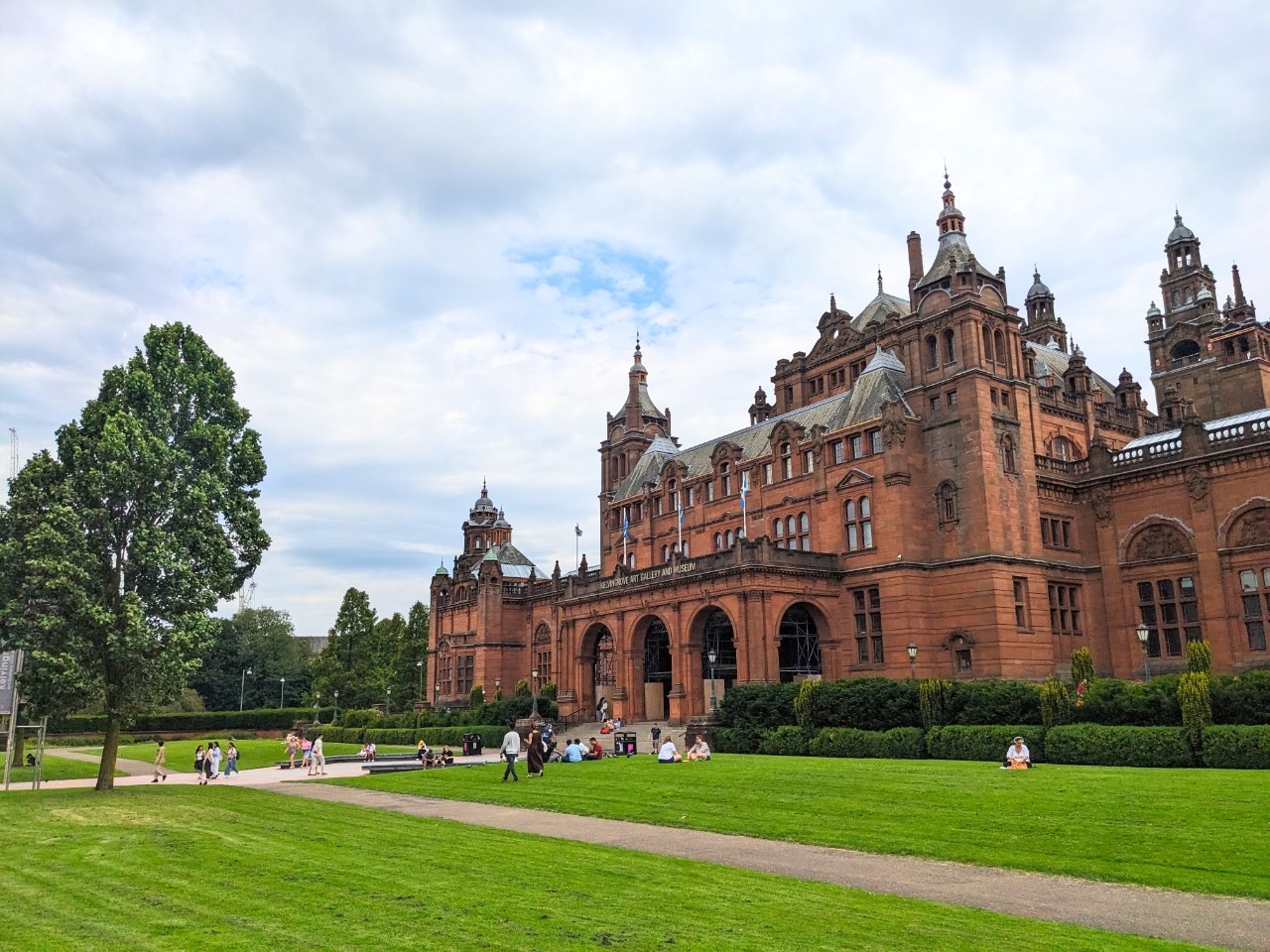 Visitors relaxing on the green lawn of Kelvingrove Park in front of the grand Kelvingrove Art Gallery and Museum