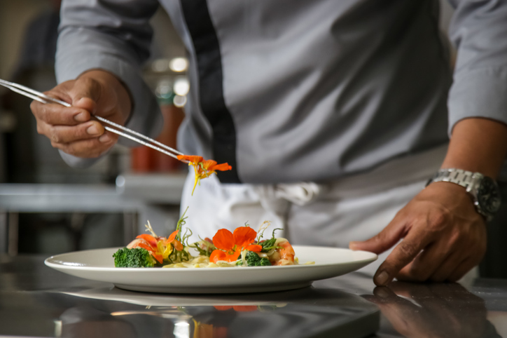 Closeup of male chef arranging edible flowers on the meal in the commercial kitchen