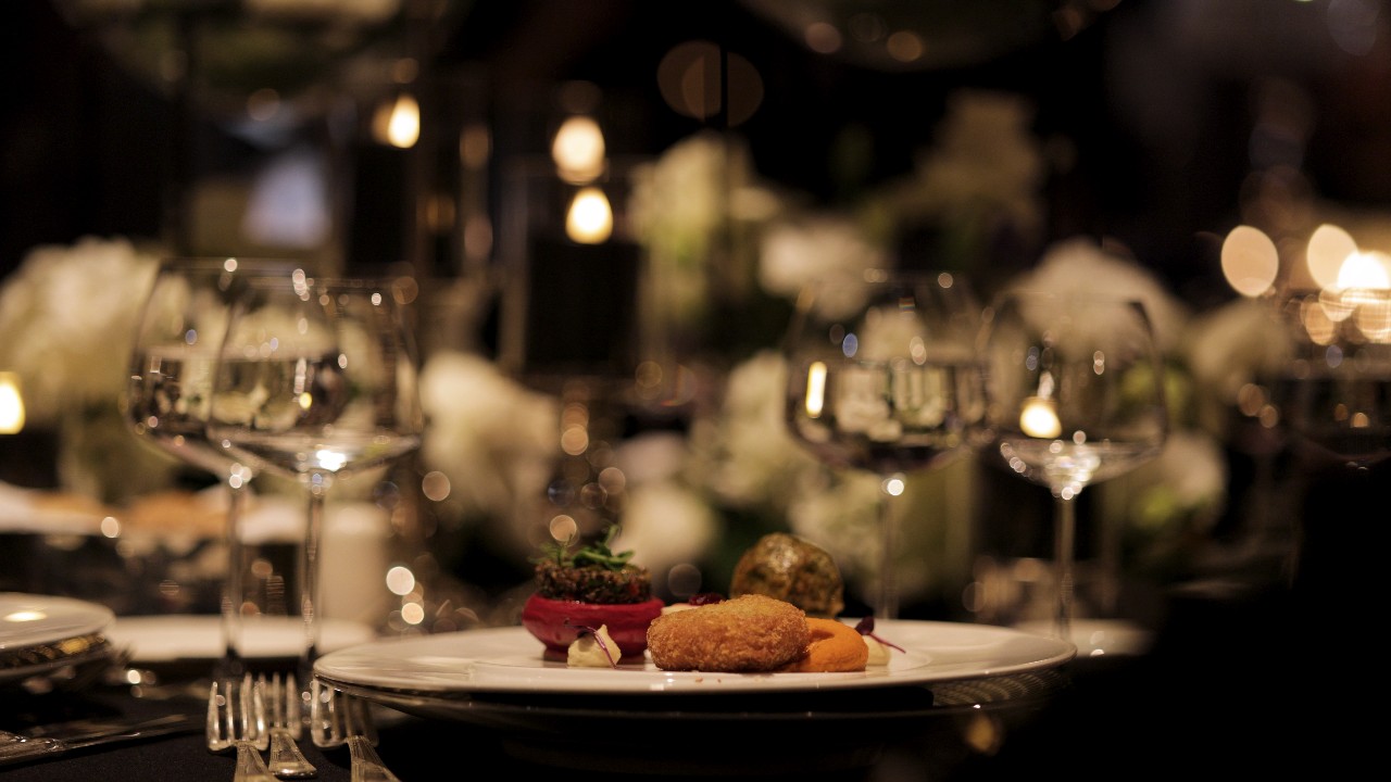A beautifully plated gourmet dish served at a sophisticated event, accompanied by fine wine and elegant table settings